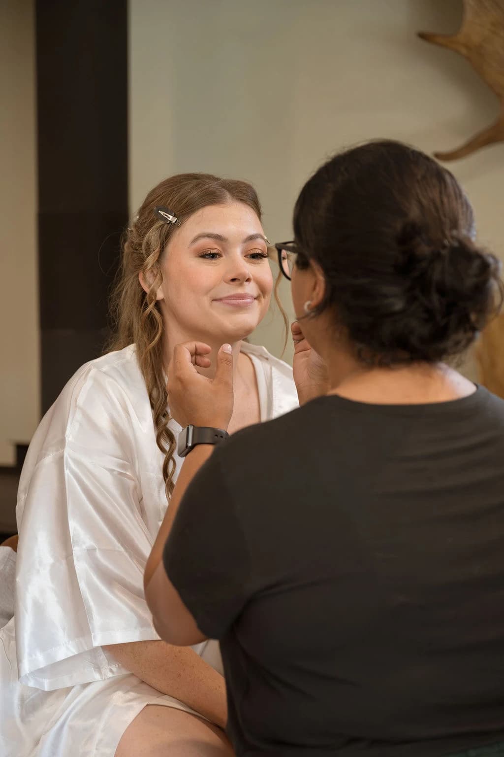 Sheena applying a complexion touch-up to a bride in a white robe.