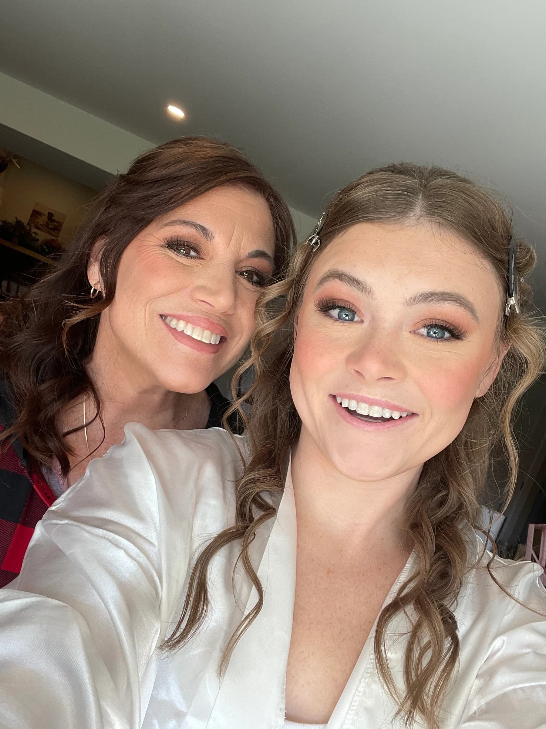 Two women smiling together with finished makeup looks.